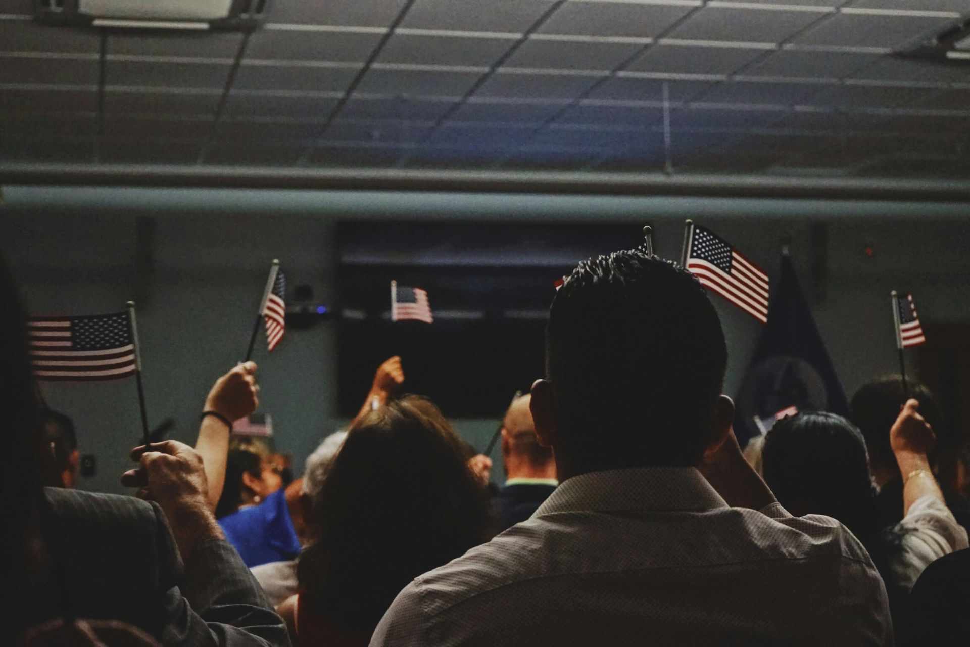 People waving American flags in a room with a light fixture and a blue and grey ceiling.