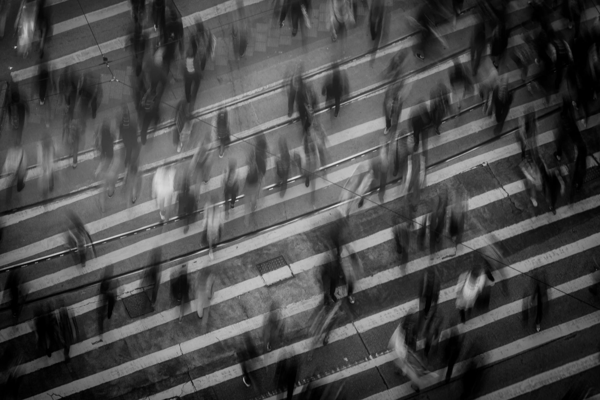 Overhead shot of pedestrians blurred while crossing a crosswalk in black and white.