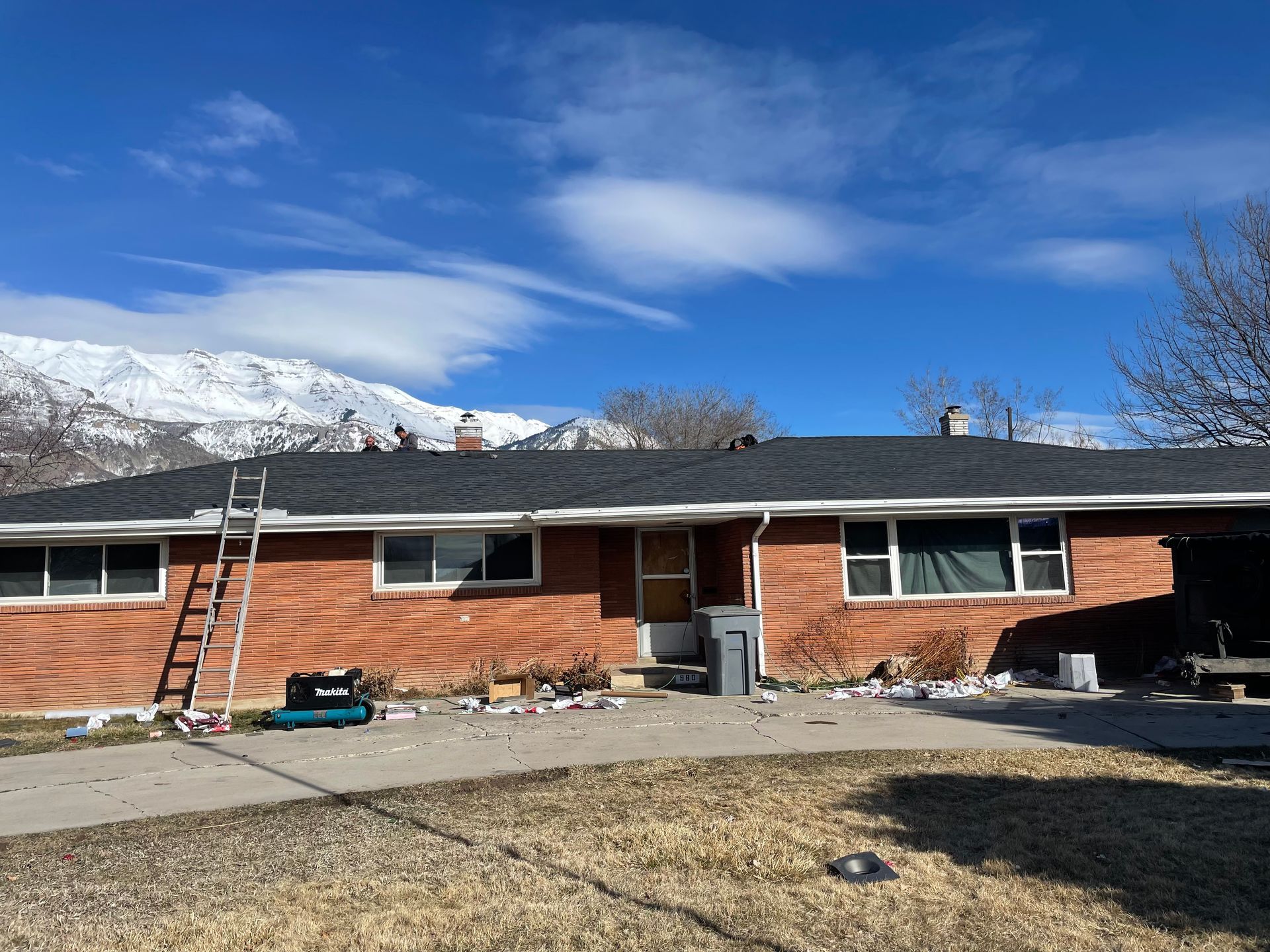 A brick house with a ladder on the roof and a snowy mountain in the background.