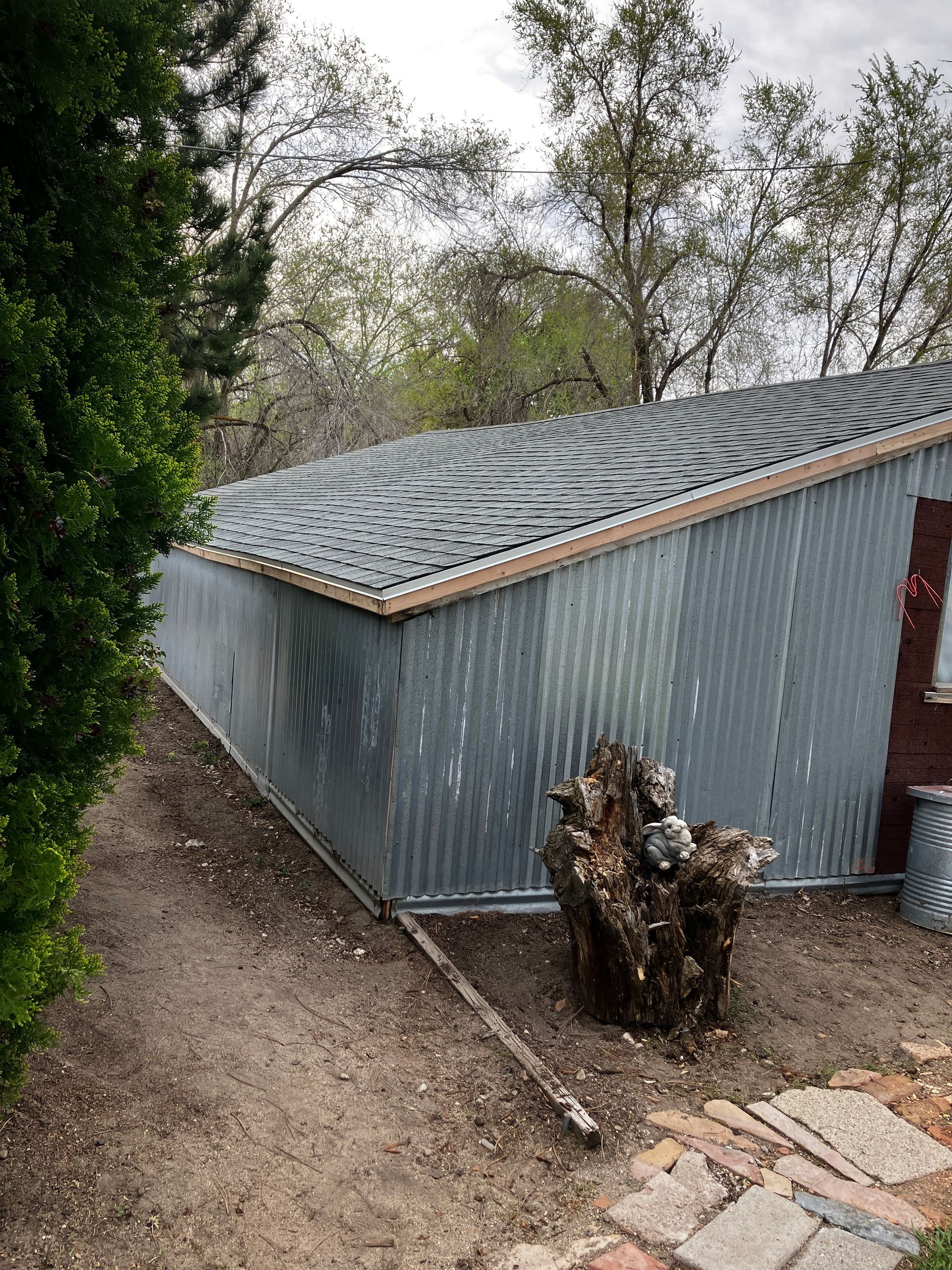 A metal shed with a roof and a tree stump in front of it.