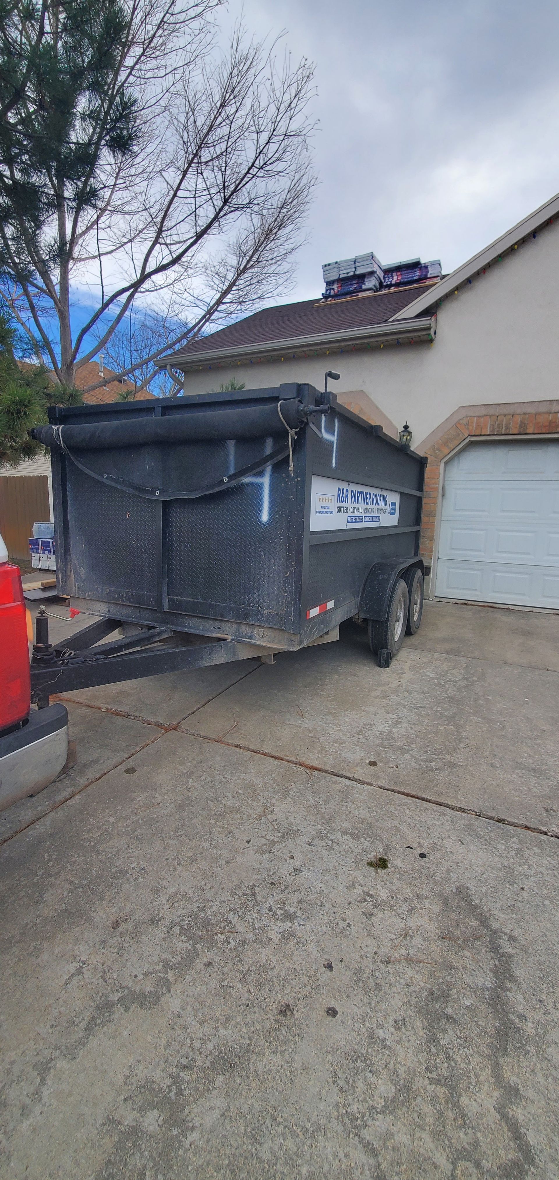 A dumpster trailer is parked in a driveway in front of a house.
