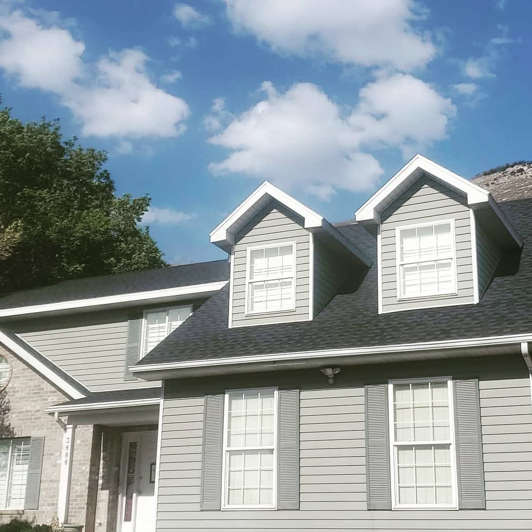 A house with a black roof and white shutters on a sunny day.