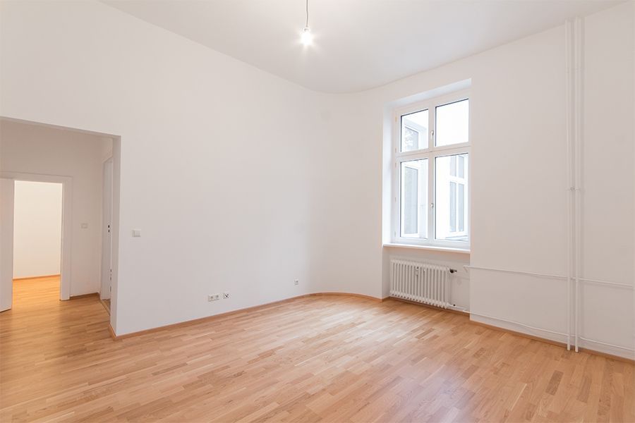 An empty living room with hardwood floors and white walls.