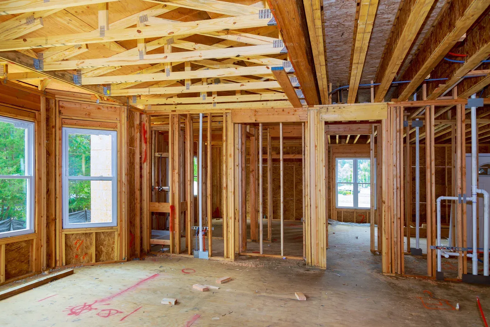 The inside of a house under construction with wooden beams and windows.