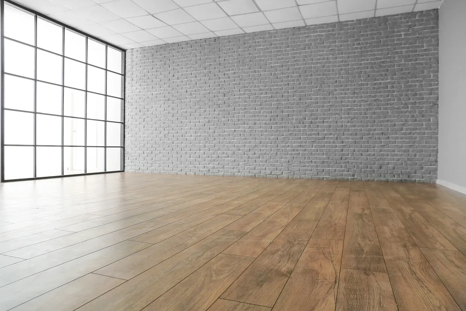 An empty room with a wooden floor and a brick wall.
