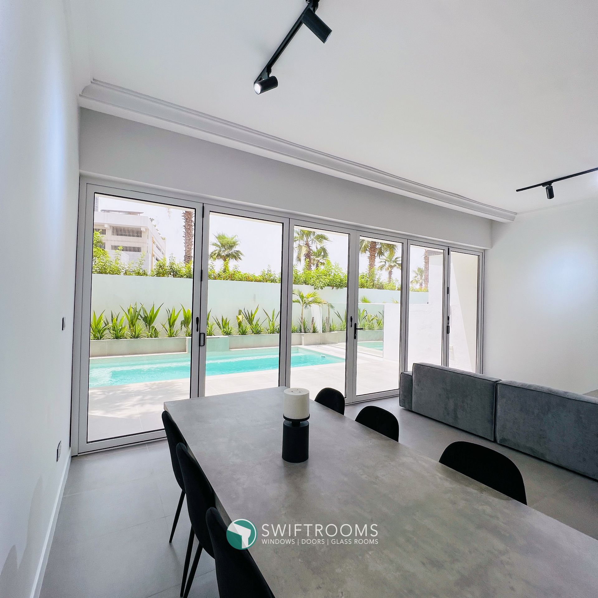 A living room with a table and chairs and a swimming pool in the background