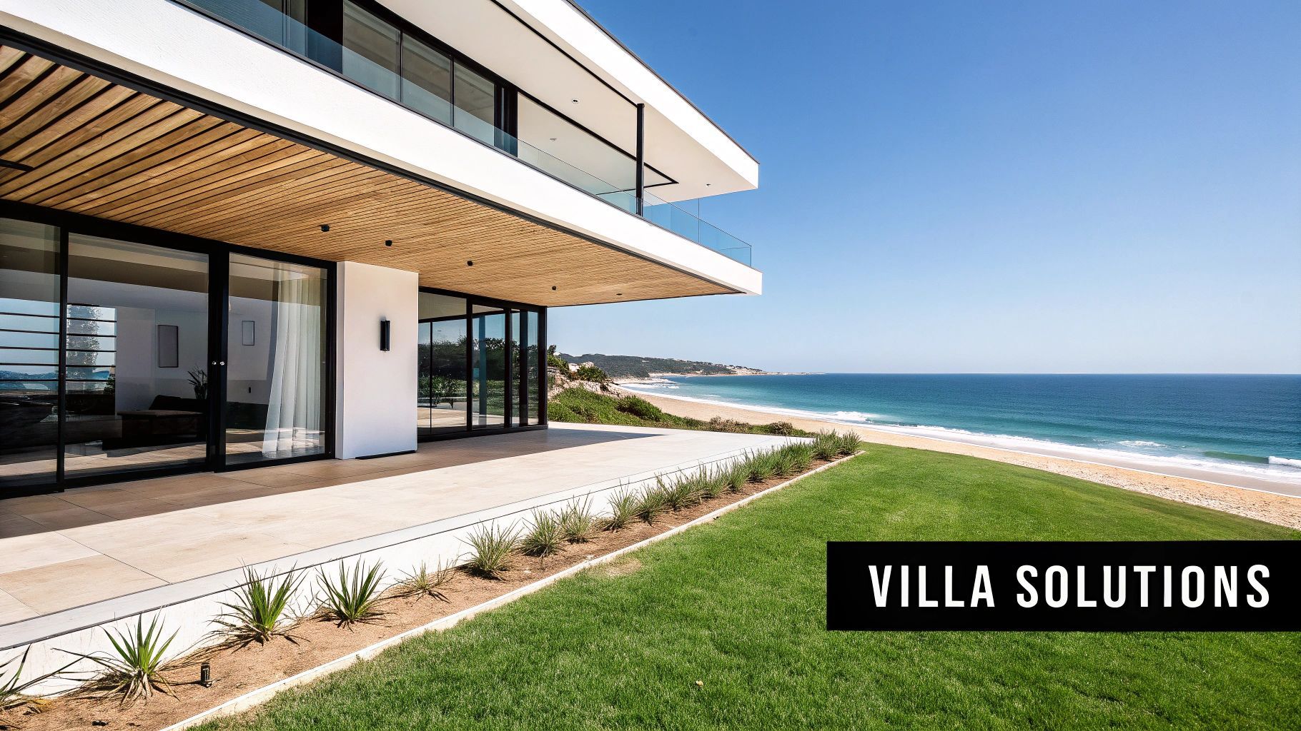 Modern beachfront villa with large windows, grassy lawn, and ocean view.