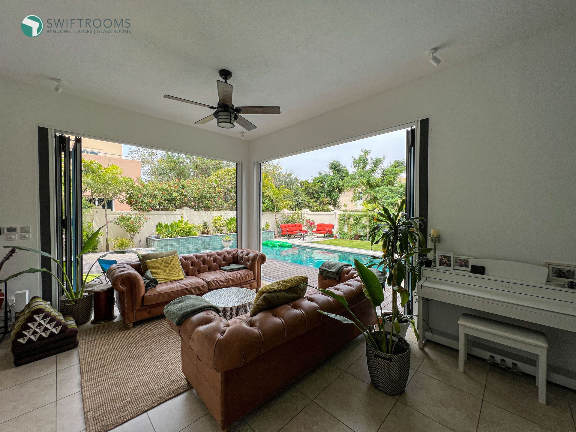 A living room with a couch , piano , and ceiling fan.