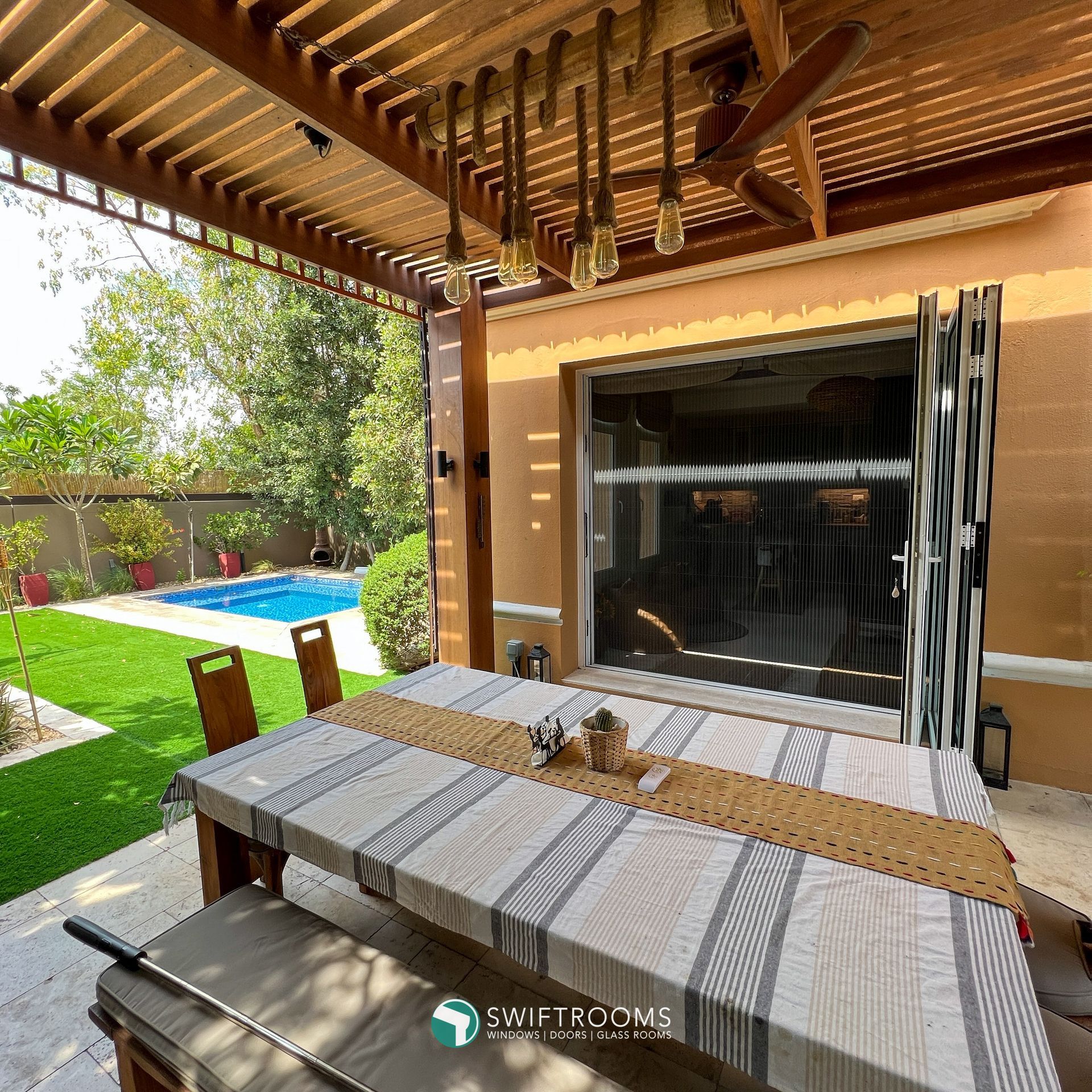 A patio with a table and chairs under a pergola with swiftroome written on the bottom