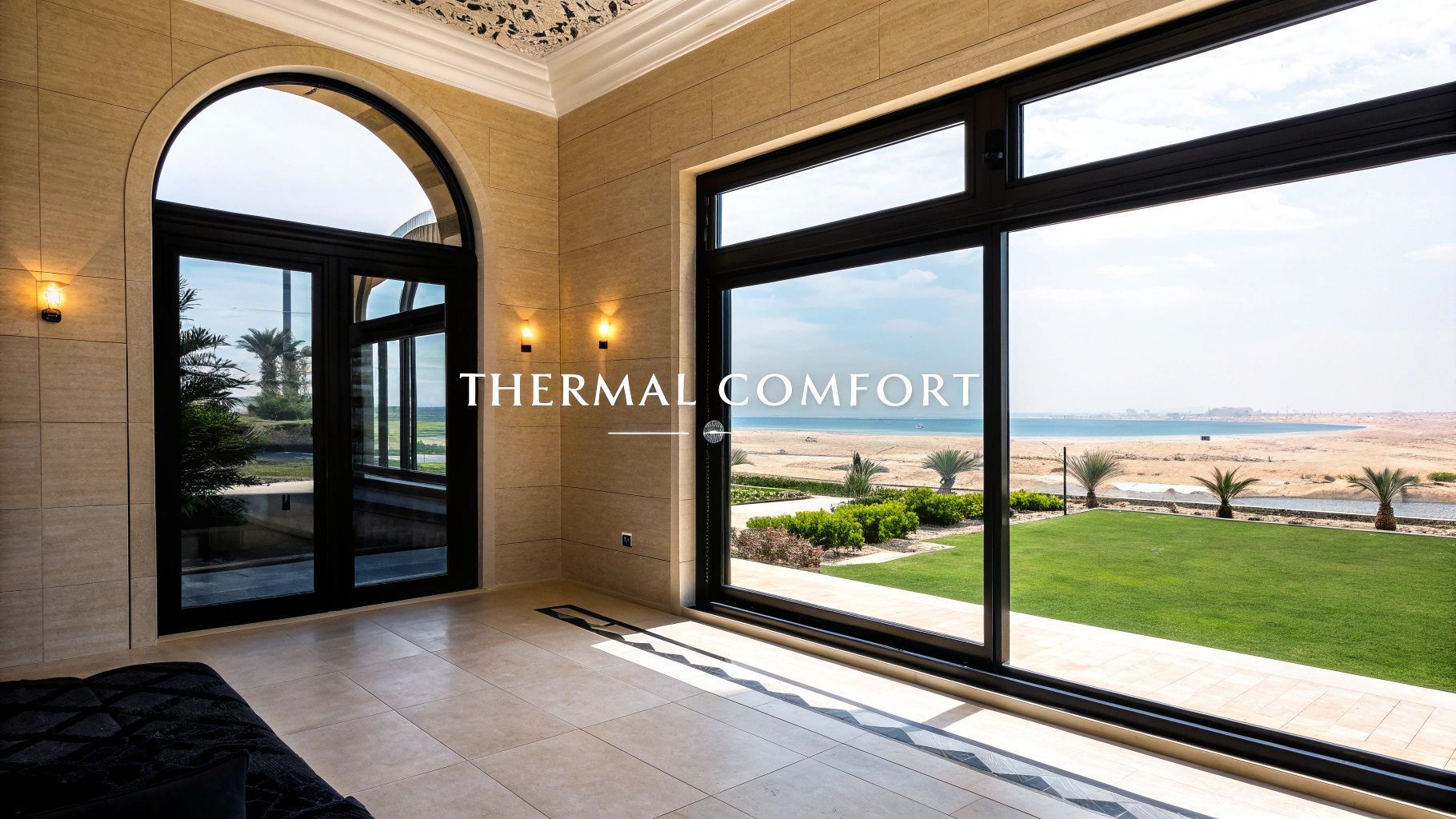 Spacious room with large windows overlooking a beachfront yard. Black framed windows, stone walls, neutral colors.