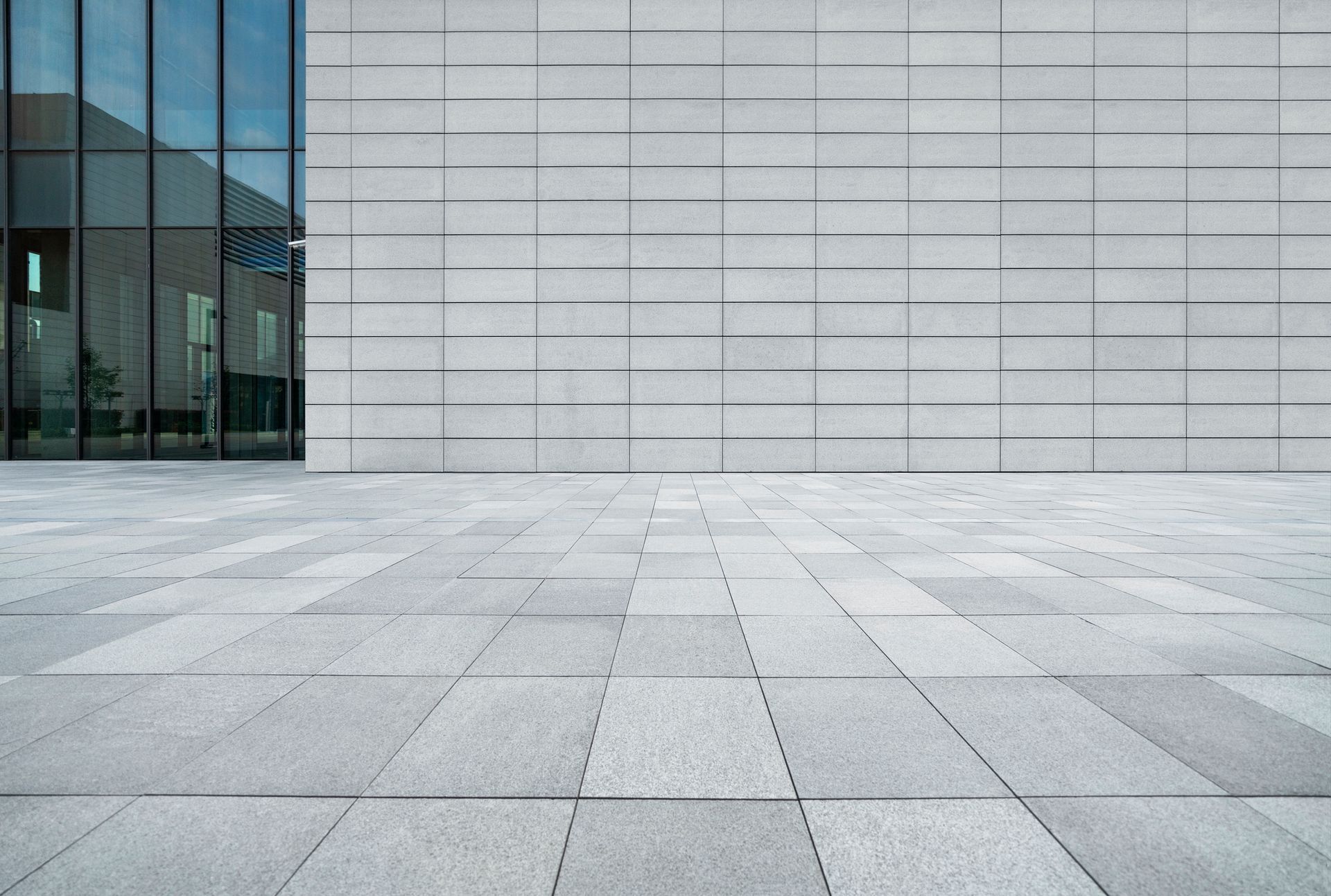 Modern building facade with glass windows and light gray tiled plaza.