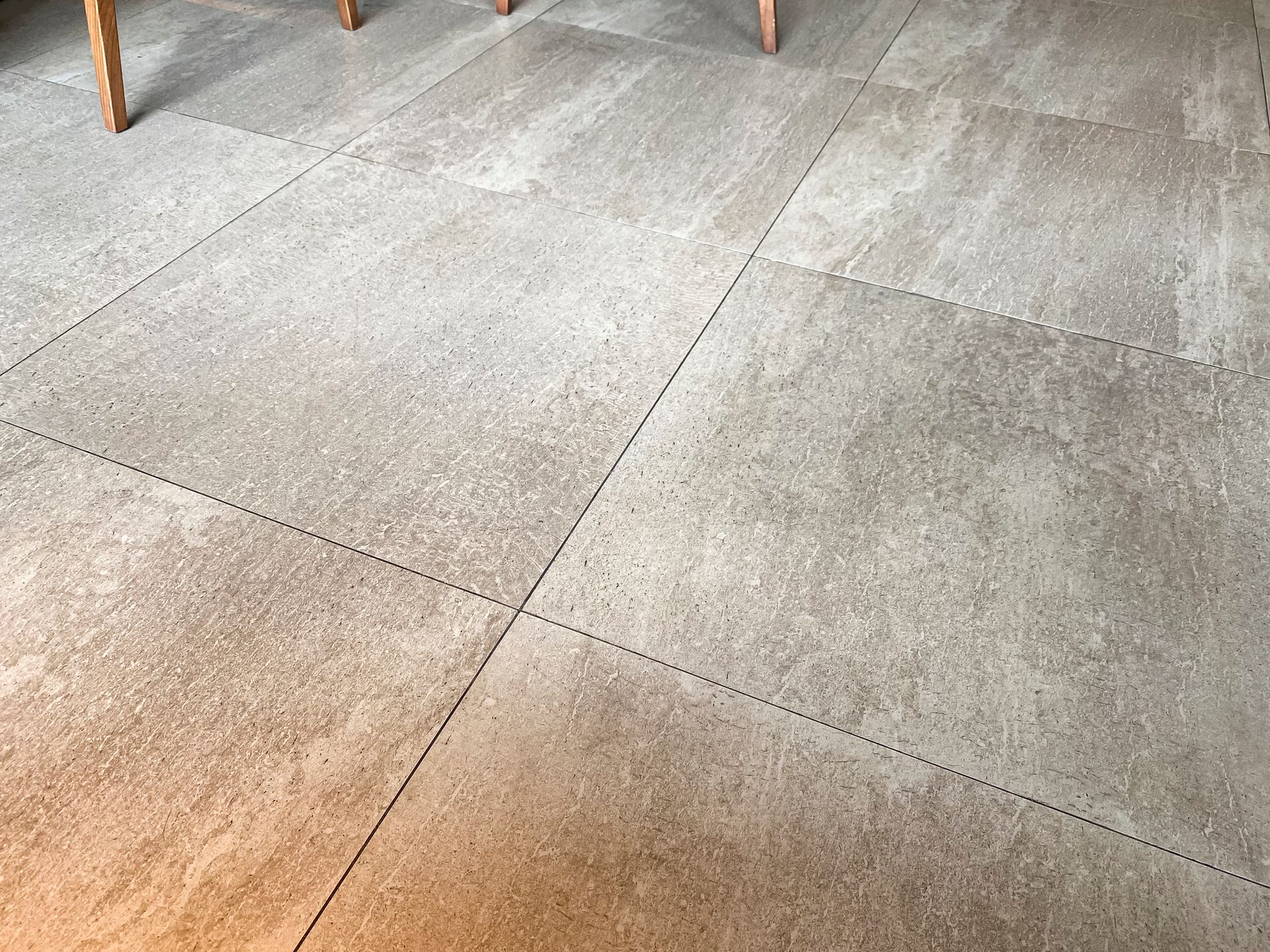 Gray, textured tiles on a floor, with dashed lines marking the tile edges. Legs of a table are visible.