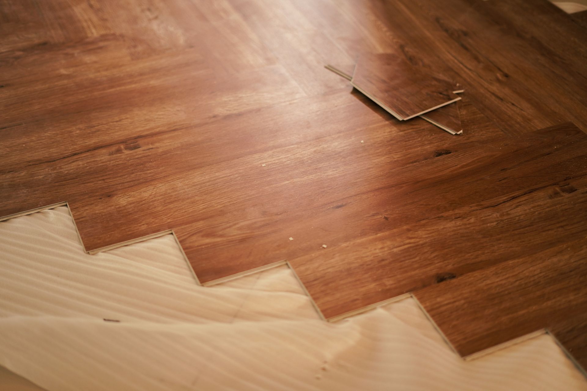 Wooden flooring being installed, pieces in a herringbone pattern with light underlayment.