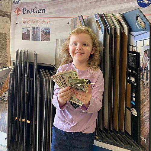 Smiling child holding cash in a flooring store, standing near product samples.