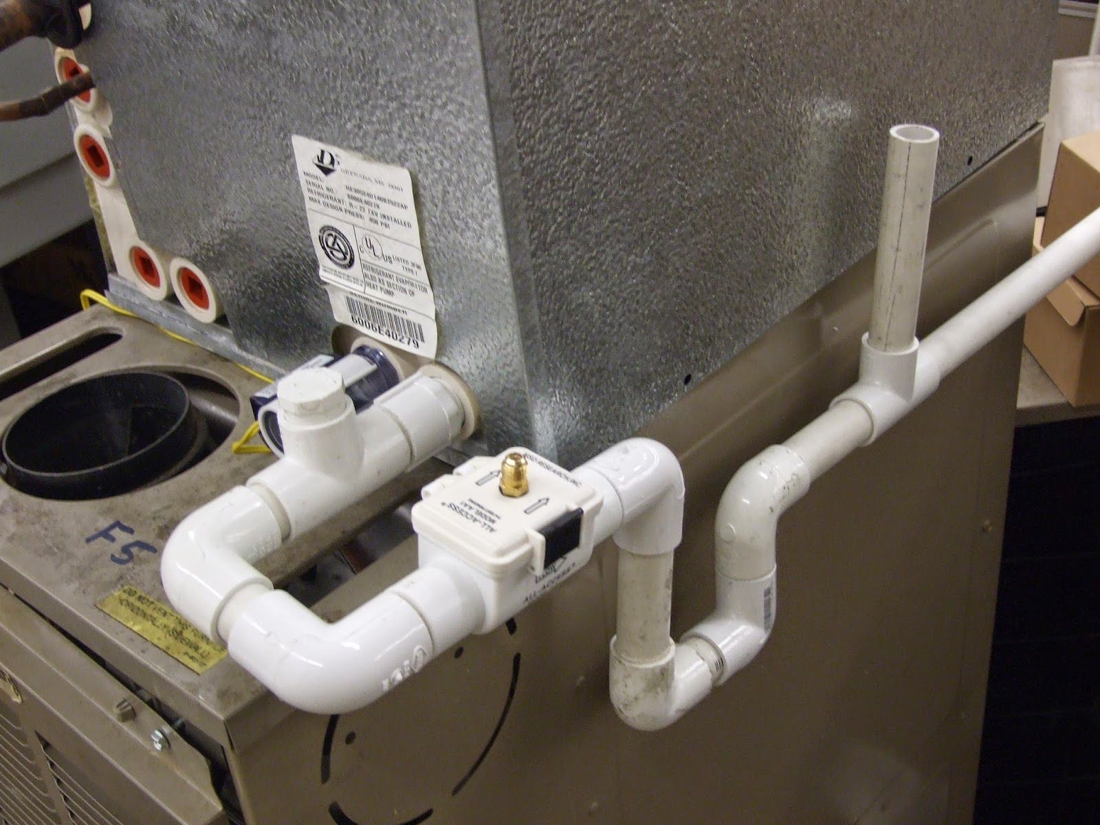 HVAC unit with white PVC piping and valves for drainage. The unit is metallic, likely indoors.
