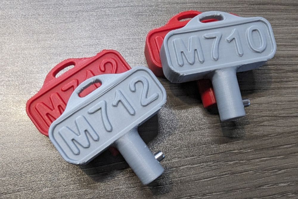 Two keys with the letters m712 and m710 on them are sitting on a wooden table.