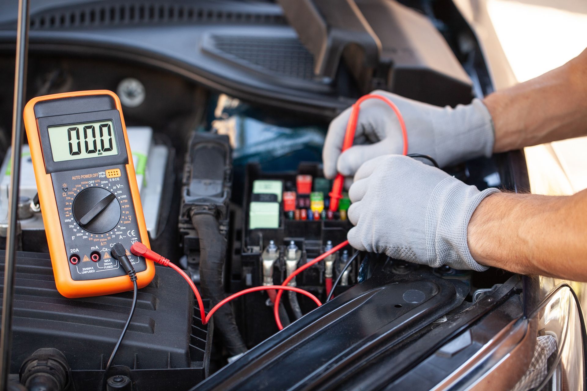 Mechanic uses a multimeter to test a car's electrical system with engine open.