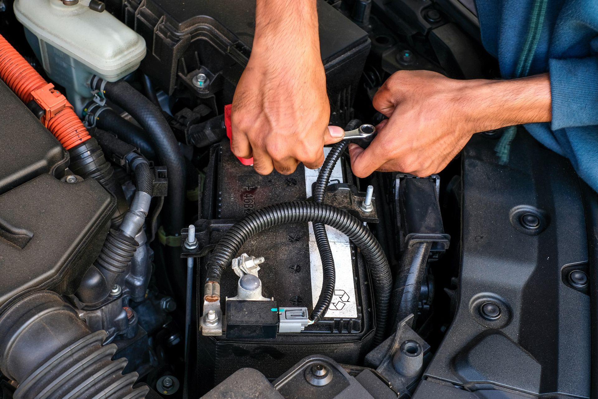 Hands using a wrench to work on a car battery in an engine bay.