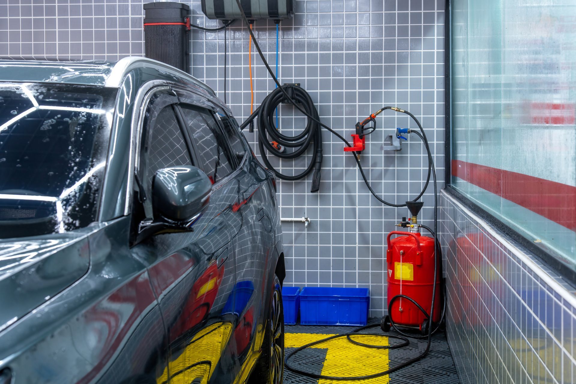 Car being washed at a car wash. A red fire extinguisher and blue toolbox sit beside it.