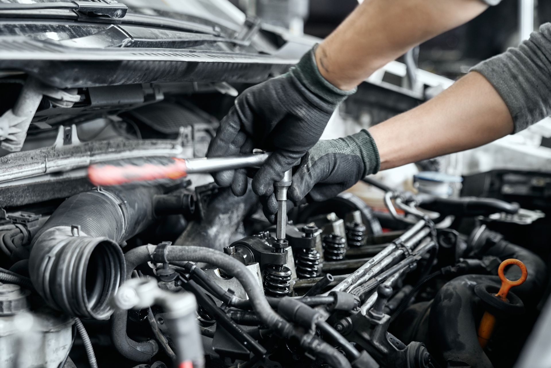 Hands in black gloves working on a car engine with a wrench.