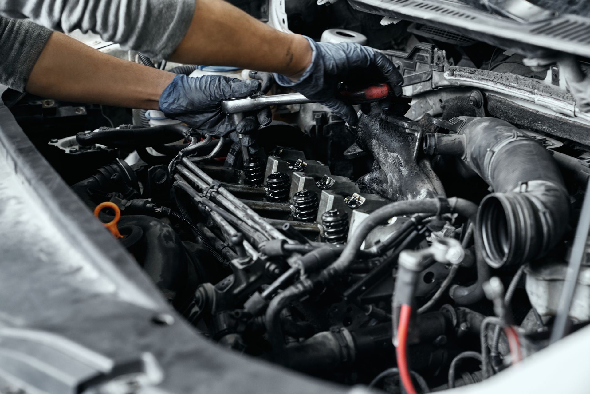 Mechanic working on car engine, wearing gloves, in a garage.