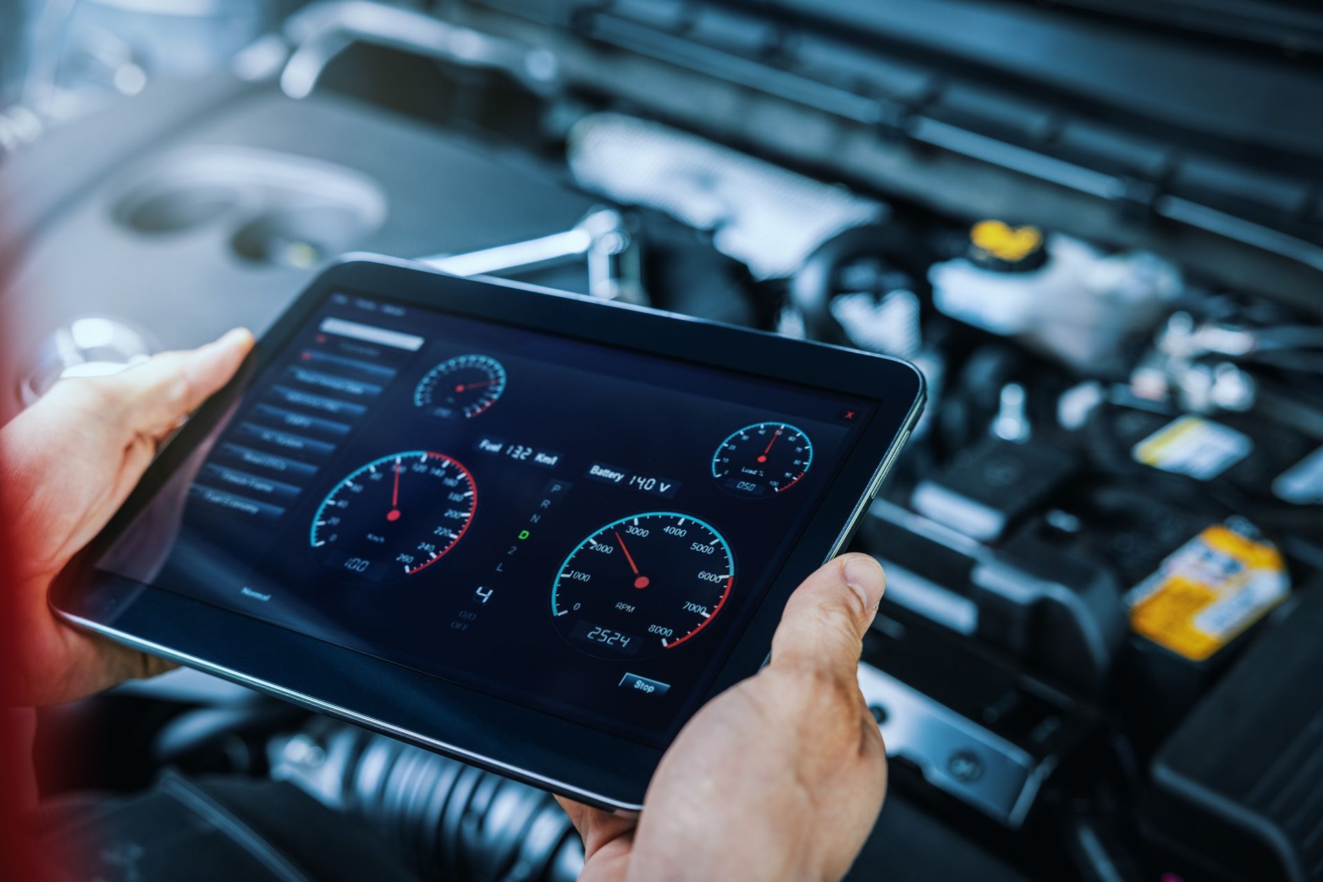 Hands holding a tablet displaying car engine diagnostics, in a vehicle's open engine bay.