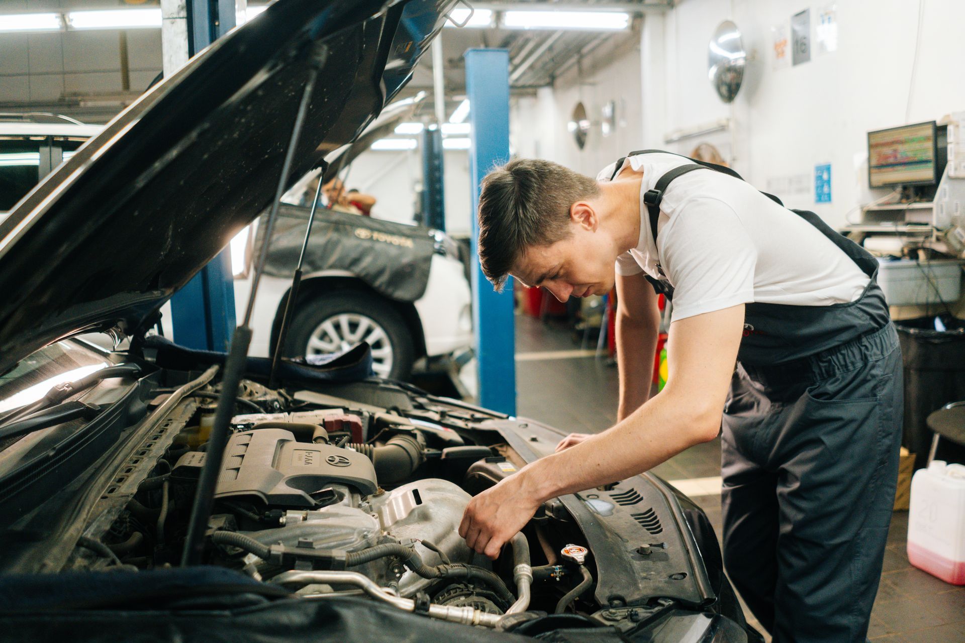 Mechanic in blue overalls working on a car engine in a garage.