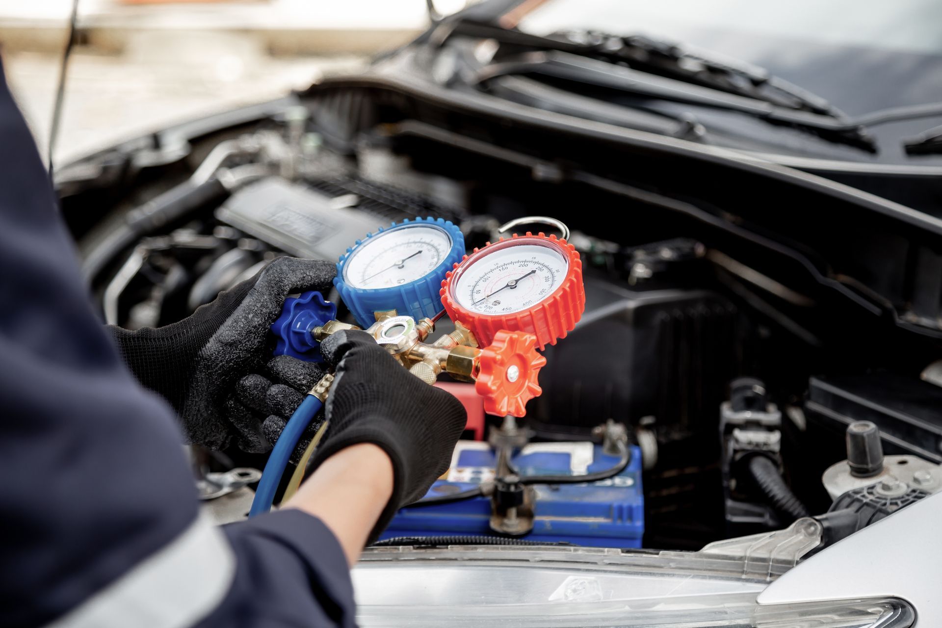 Gloved hand connects gauges to a car's engine. Red and blue gauges visible under an open hood.
