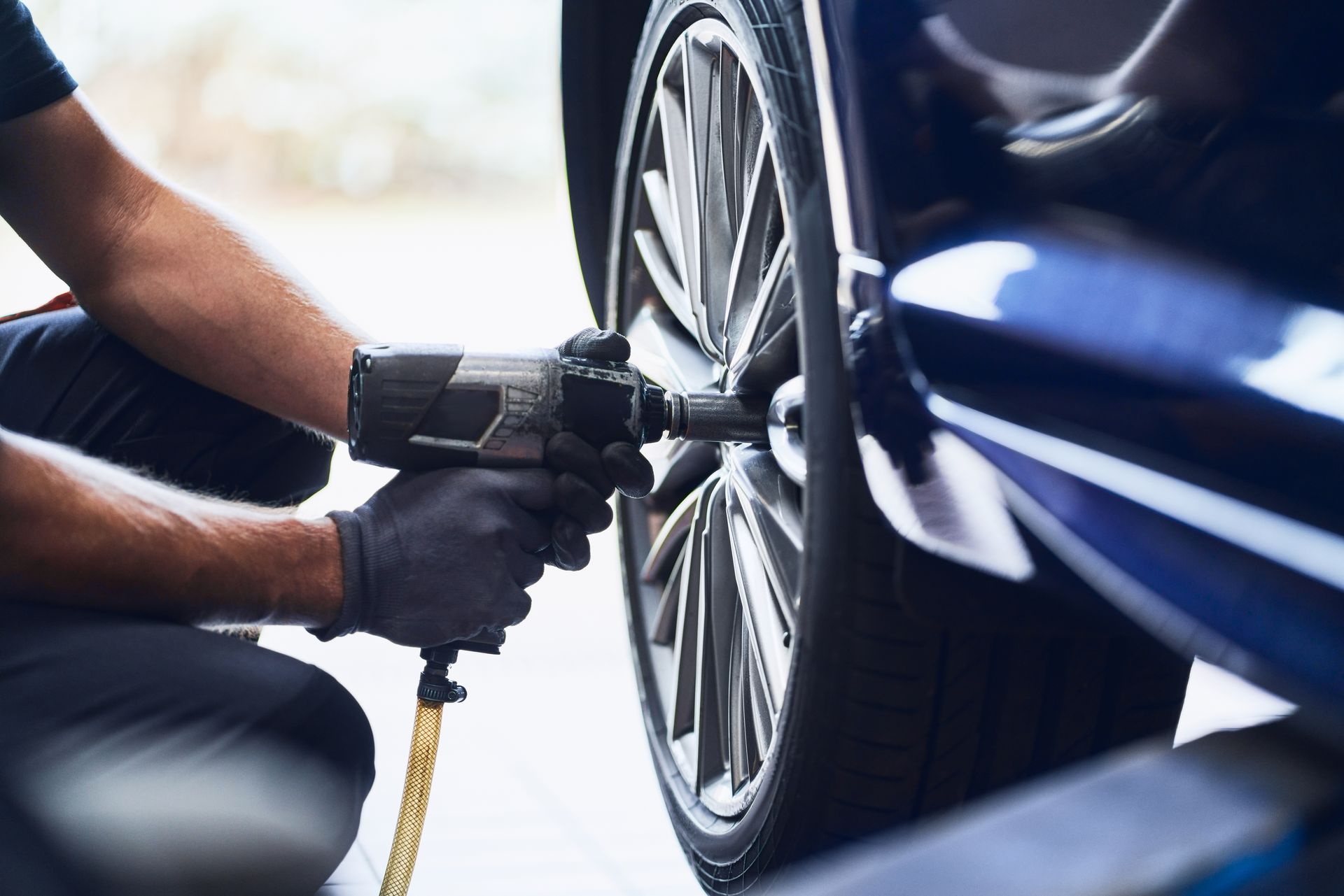 Mechanic uses an impact wrench to remove a wheel from a blue car in a garage.