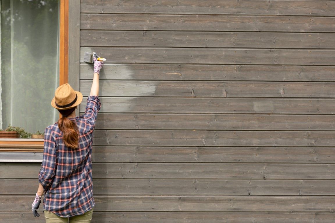 A woman is painting a wooden wall with a brush.
