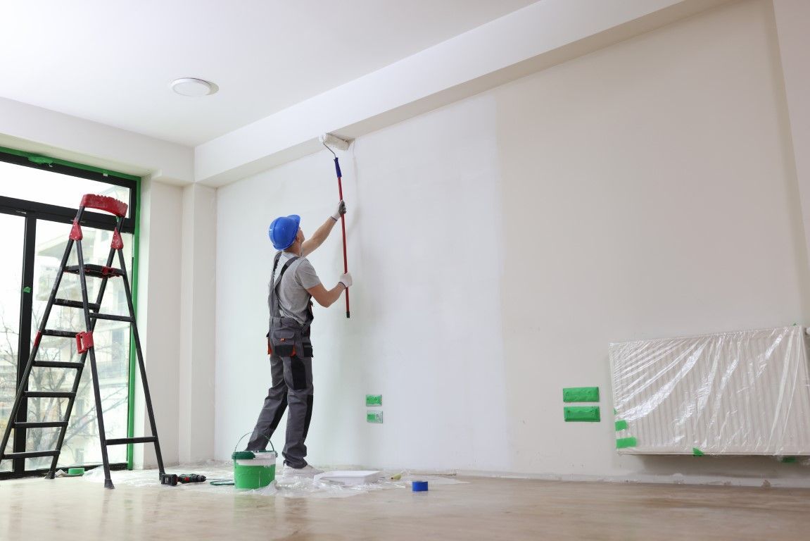 A man is painting a wall with a roller in an empty room.