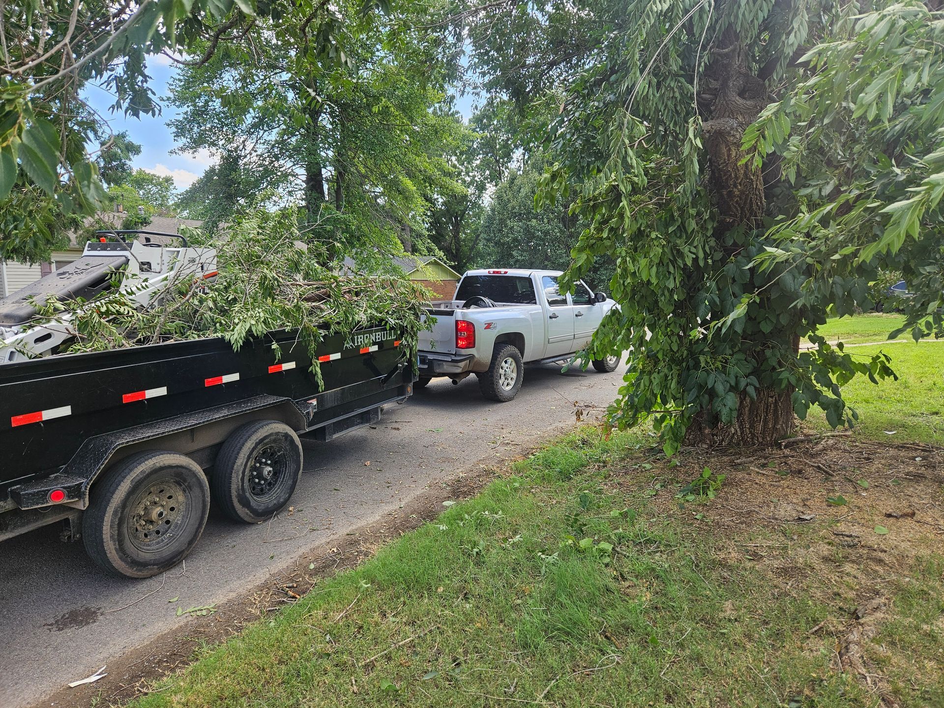 A truck is towing a dumpster down a road next to a tree.