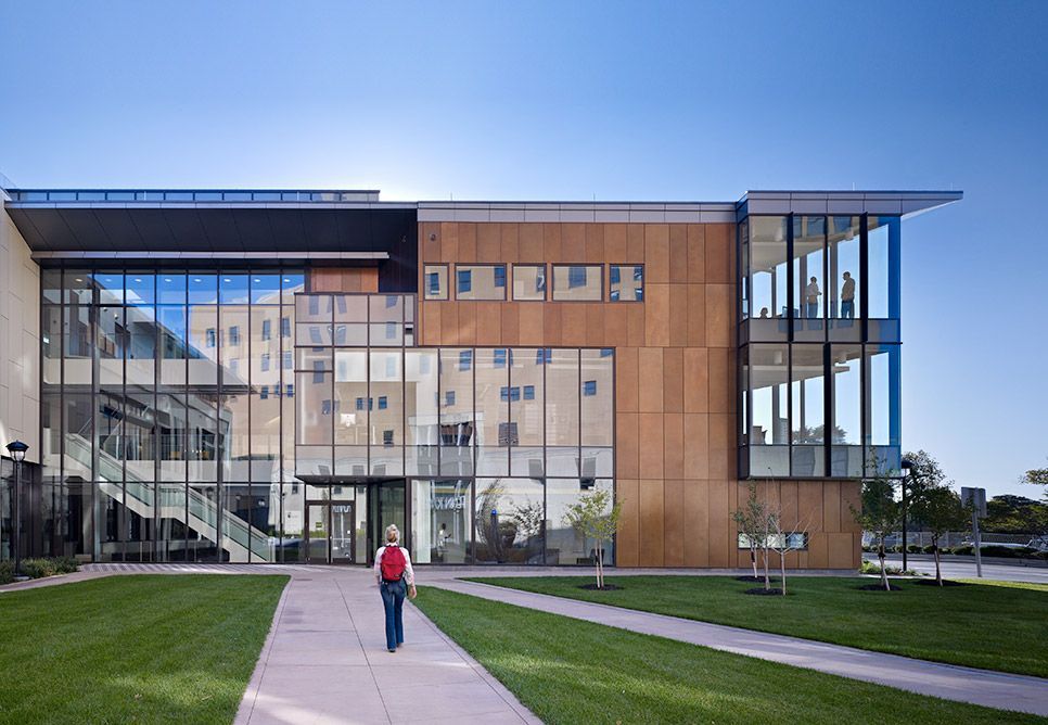 A woman is walking down a sidewalk in front of a large building.