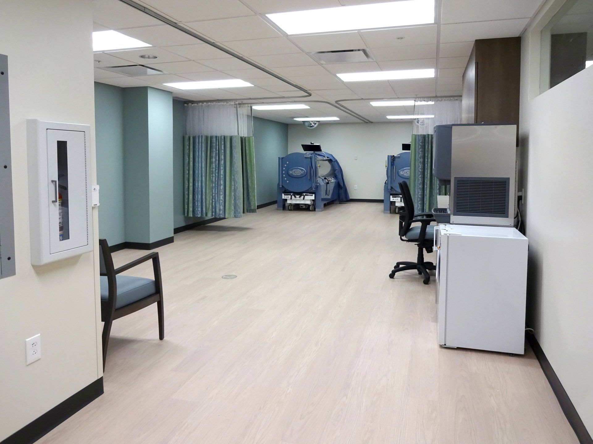 An empty hospital room with a chair and a refrigerator