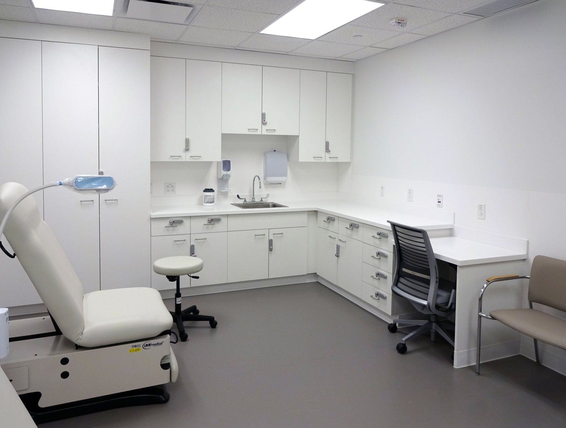 A doctor 's office with a chair a desk and a sink