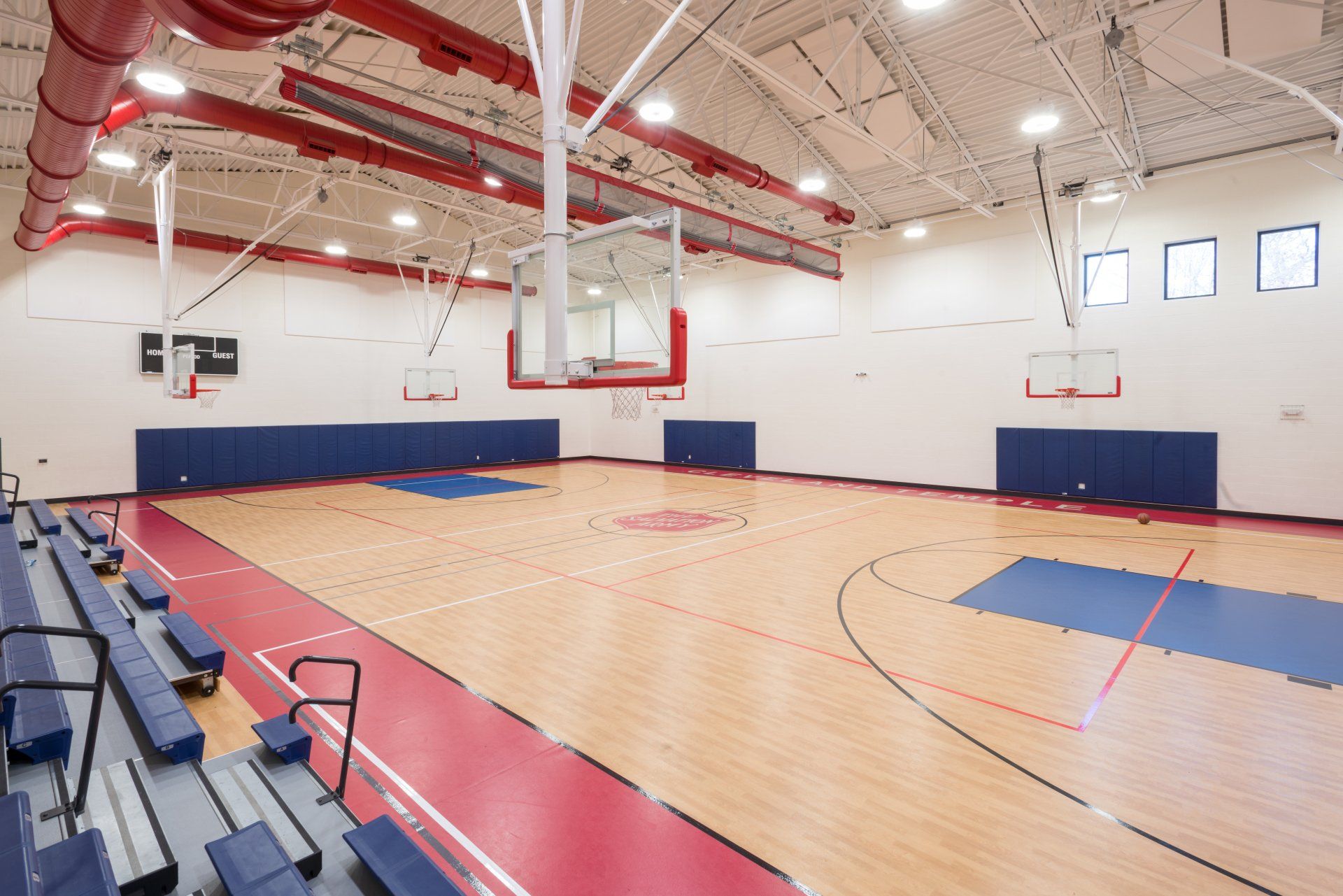A basketball court in a gym with bleachers and a basketball hoop.