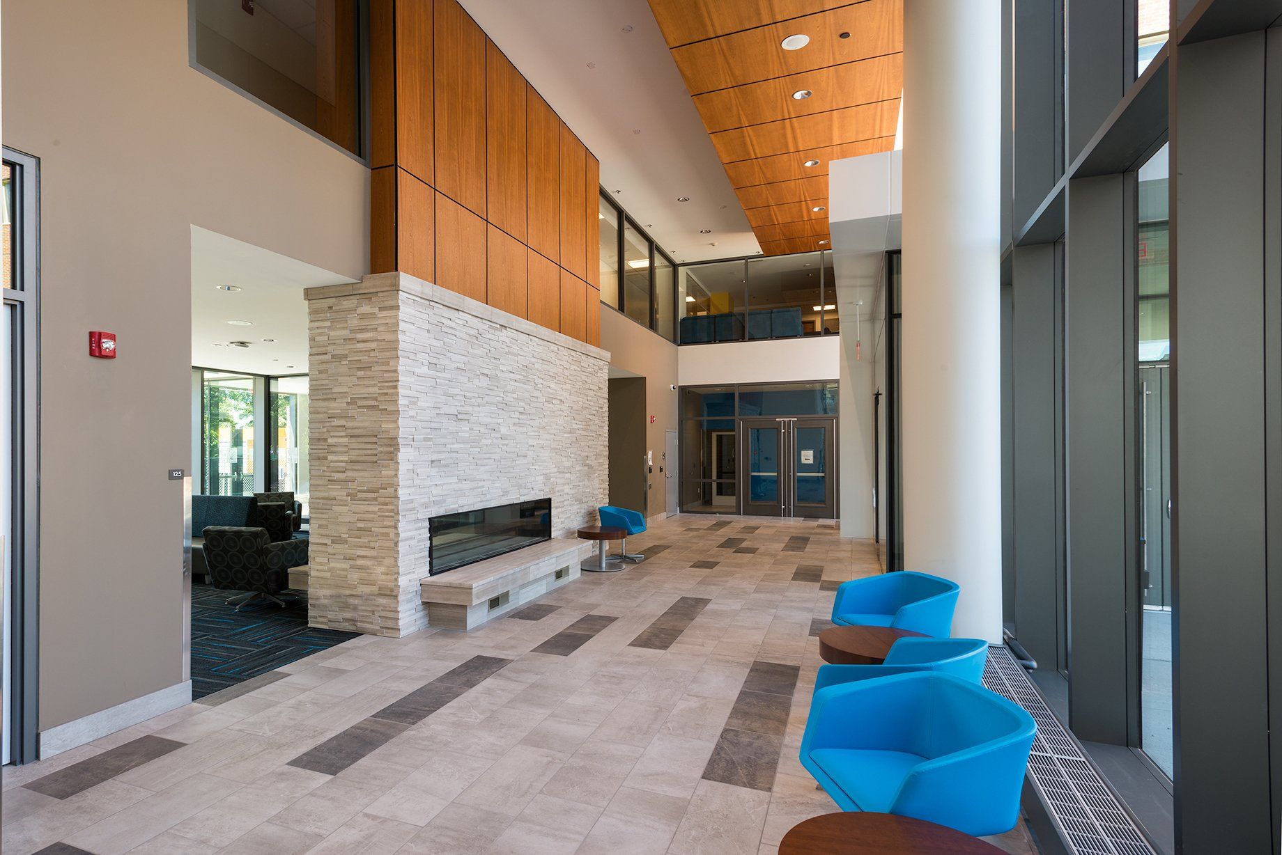 A large lobby with blue chairs and a fireplace.