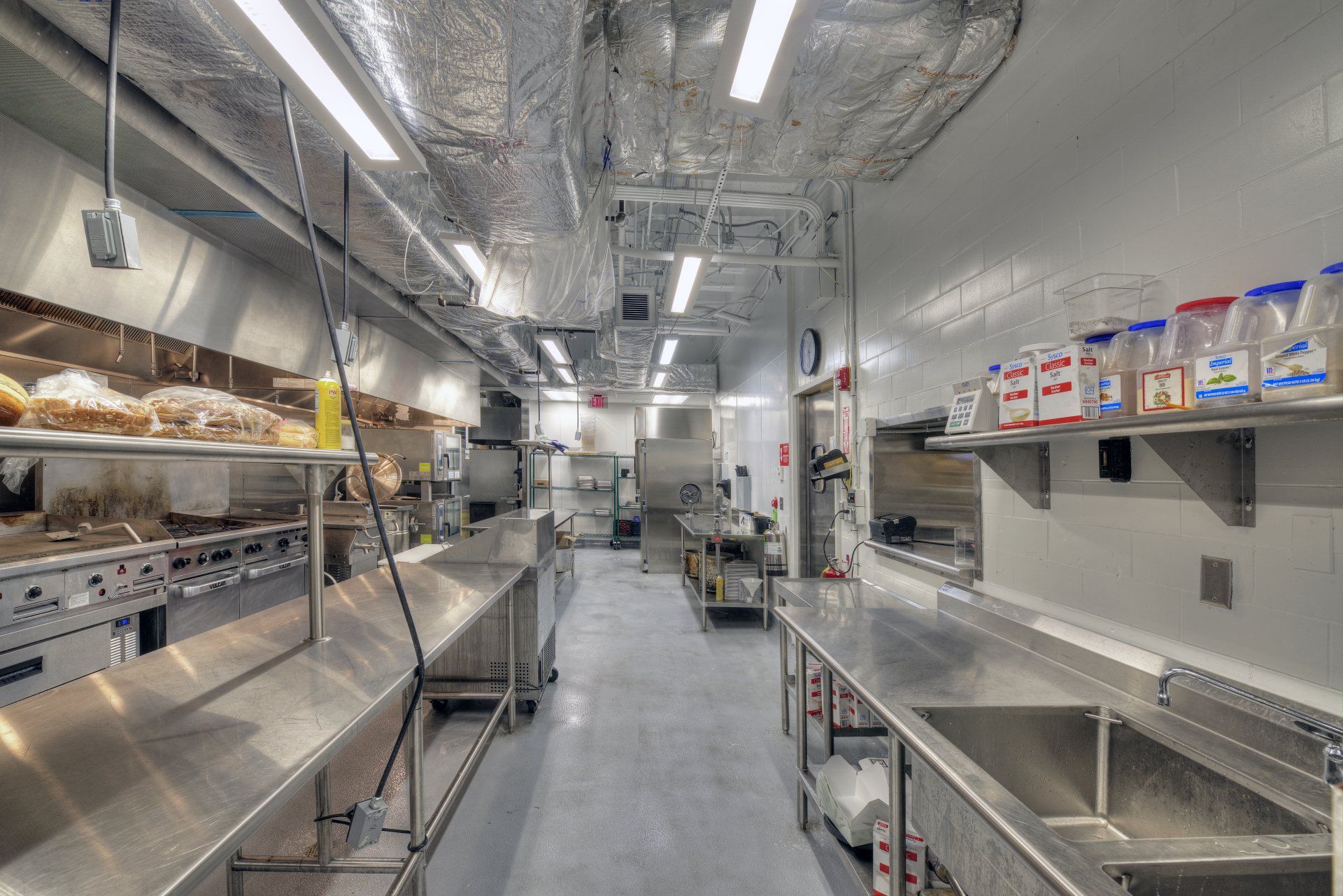 A long kitchen with stainless steel counter tops and sinks.