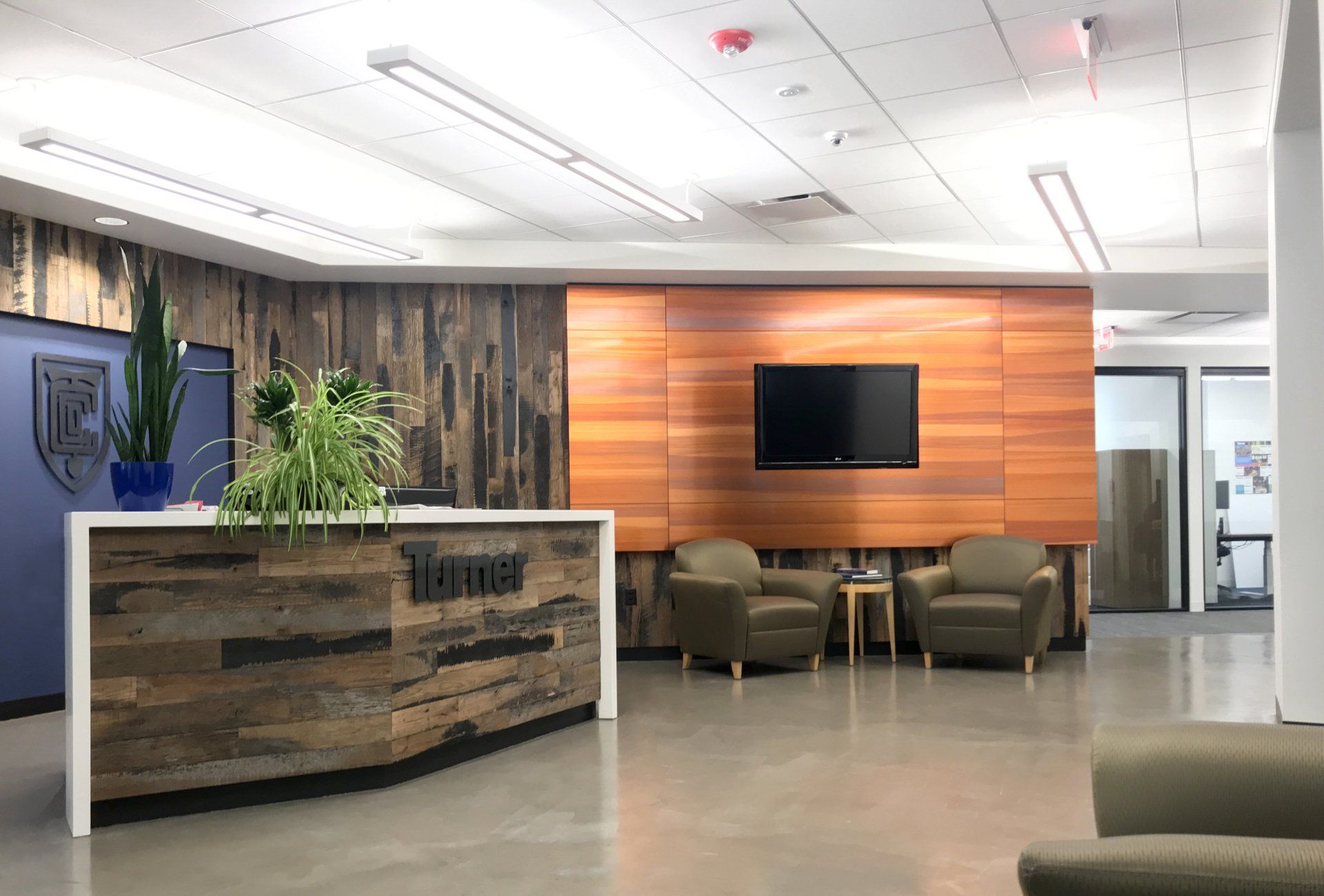A large lobby with a wooden reception desk , chairs , and a flat screen tv.