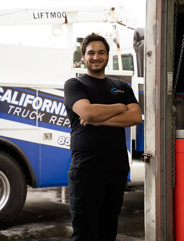 A smiling person stands with arms crossed in front of a white and blue California Truck Repair service vehicle. | Kensington Motor Cars