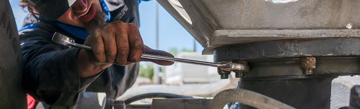 A person using a wrench to tighten a bolt on a metal machine. Hands are dirty. | California Coast Truck Repair