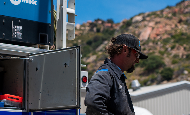 Man in workwear near open utility truck with mountainous backdrop. |  California Coast Truck Repair