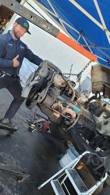 Man wearing hat and work clothes near an open truck compartment with welding equipment against a mountain backdrop. | California Coast Truck Repair