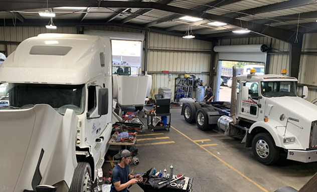 A person works on a semi-truck in an indoor repair shop where another truck is parked nearby. |  California Coast Truck Repair