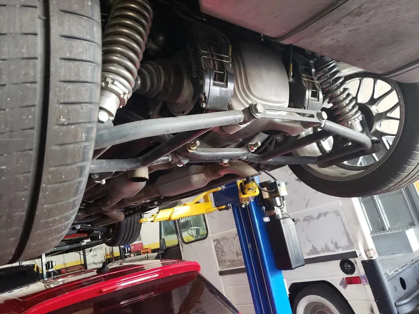 Undercarriage of a red sports car lifted in a garage. Visible are the tires, suspension, and rear axle components.