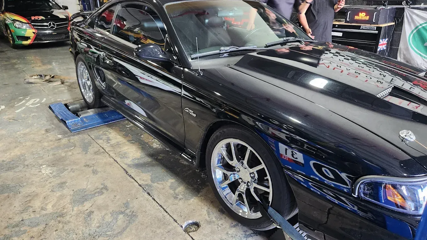 Black Mustang on a dyno being tested inside a garage. The car has chrome wheels.