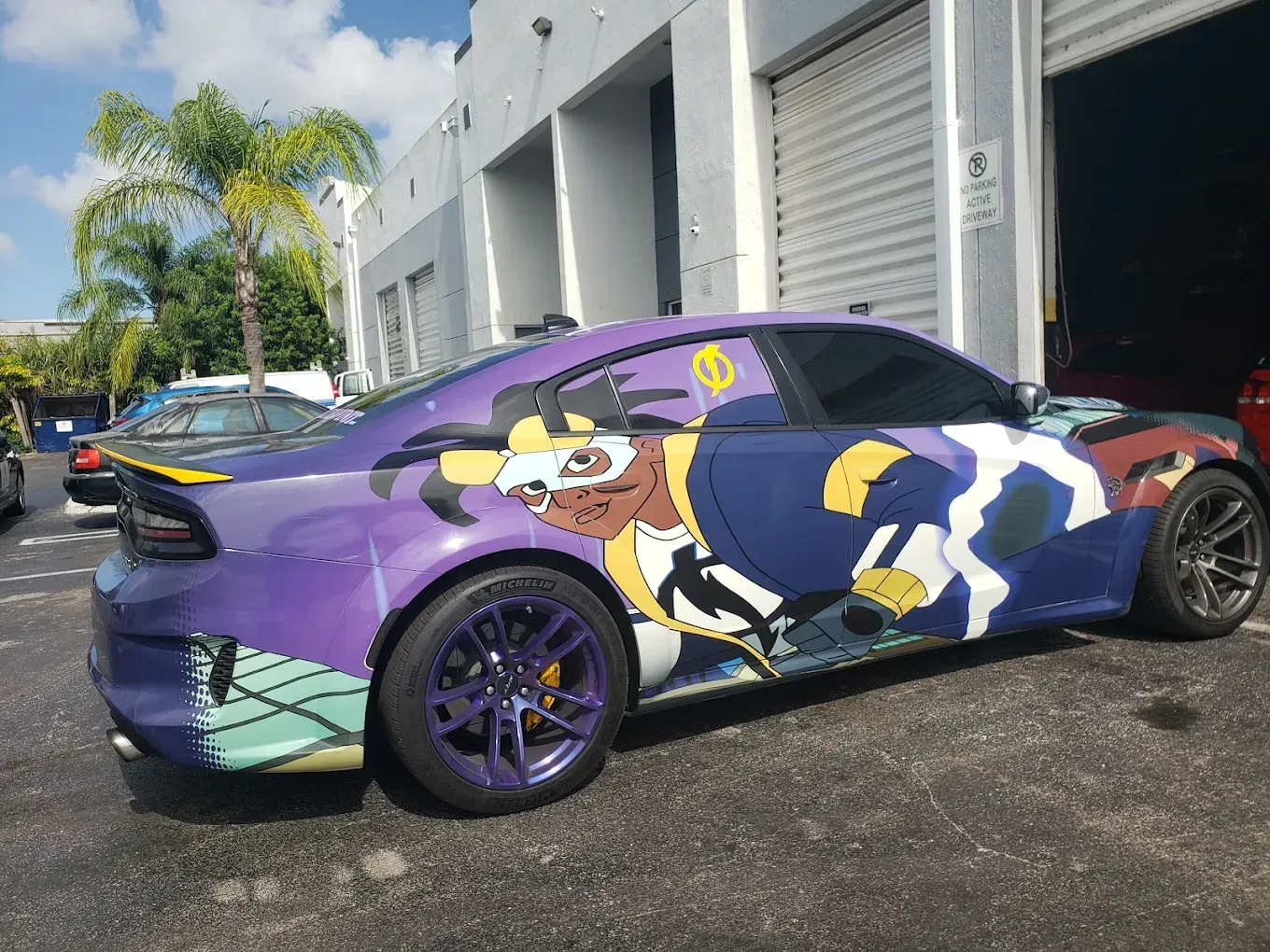 Purple Dodge Charger with anime-style graphics and purple rims, parked outside a commercial building.
