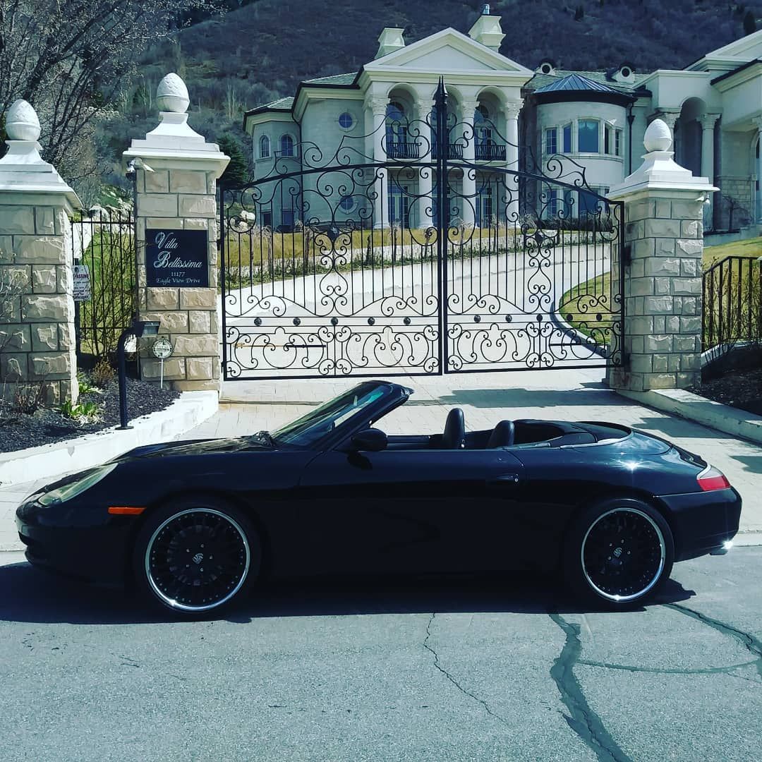 A black convertible is parked in front of a gated entrance to a mansion