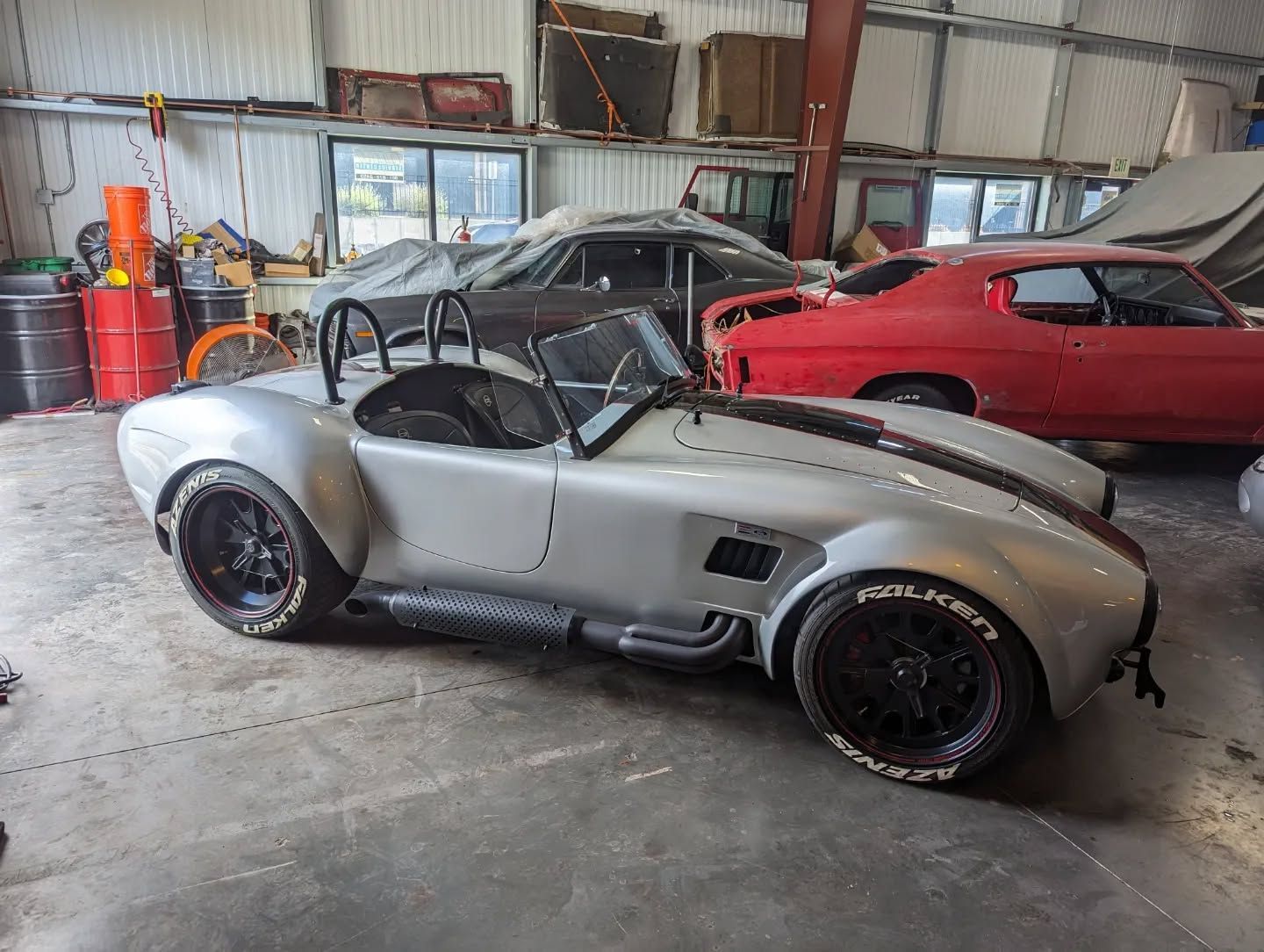 A silver sports car is parked in a garage next to a red car.