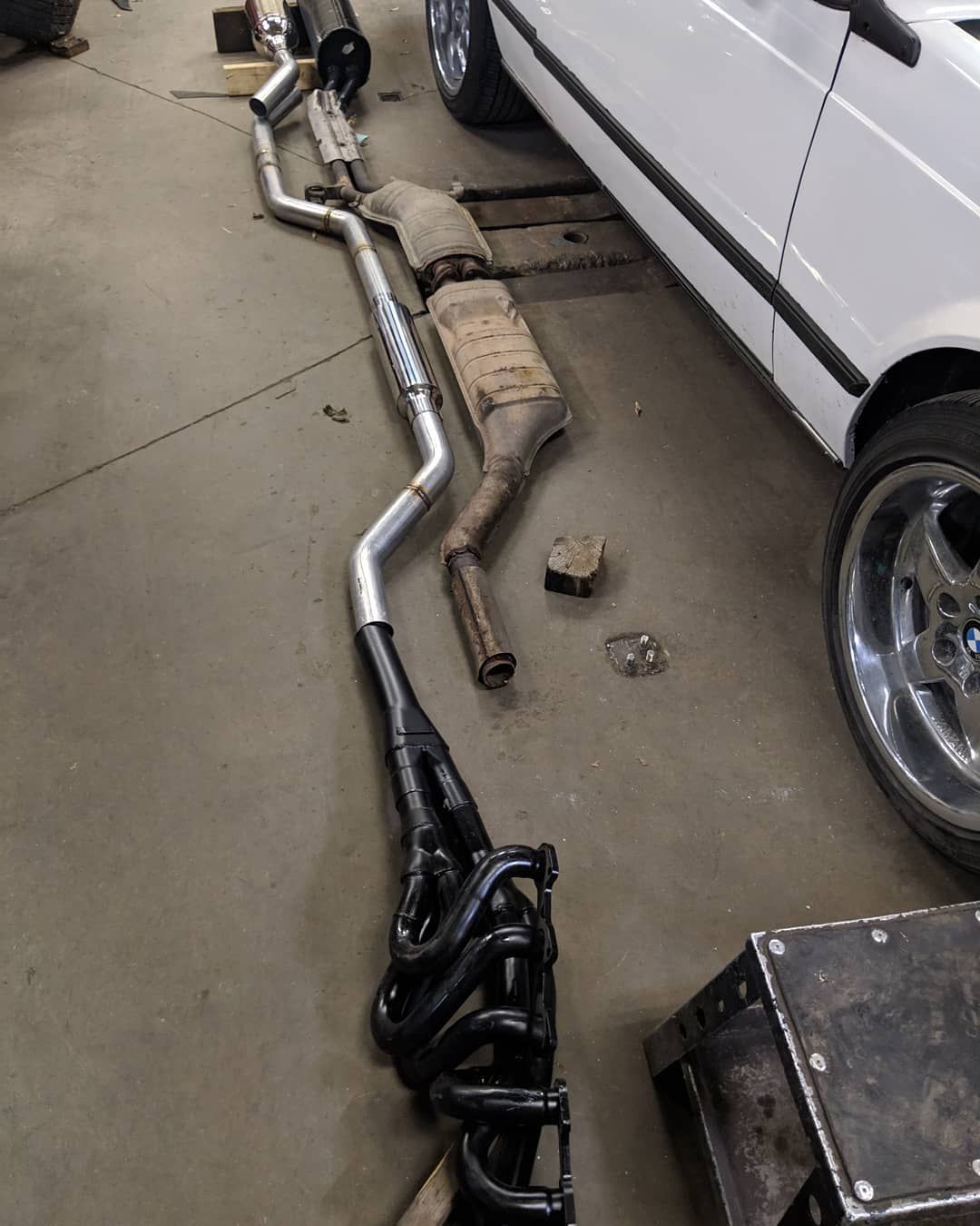 Exhaust pipes are laying on the ground next to a white car